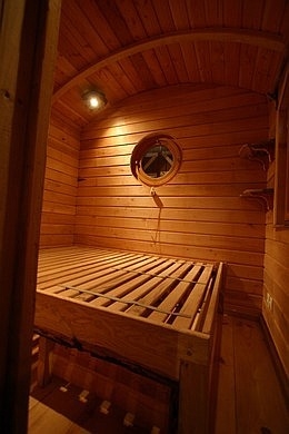 Chambre de la roulotte avec le lit artisanal, son sommier en bois et ses tiroirs coulissants en dessous.